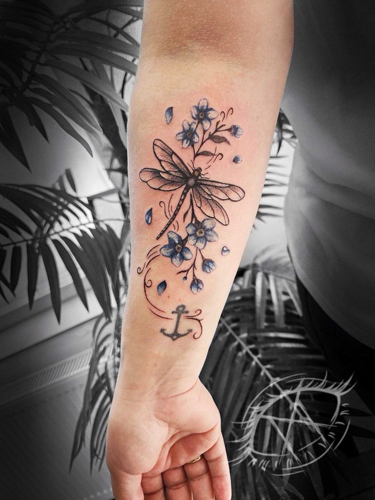 Tattoo von Kyra: Libelle, Blüten und kleiner Anker am Unterarm